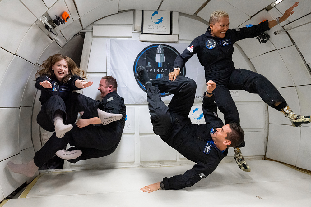 The 4 crew members of Inspiration4, inside the cabin of a Zero-G airplane. The four crew members are in various states tumbling through the shuttle