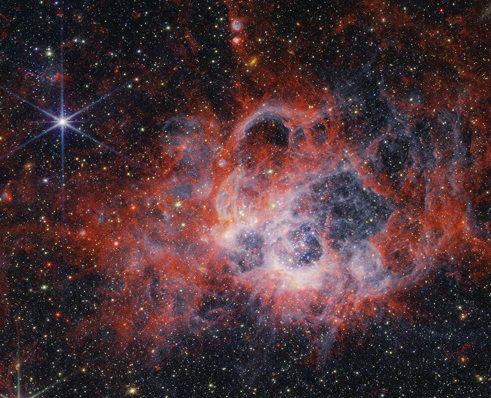 At the centre of the image is a nebula on the black background of space. The nebula is composed of clumpy, red, filamentary clouds.