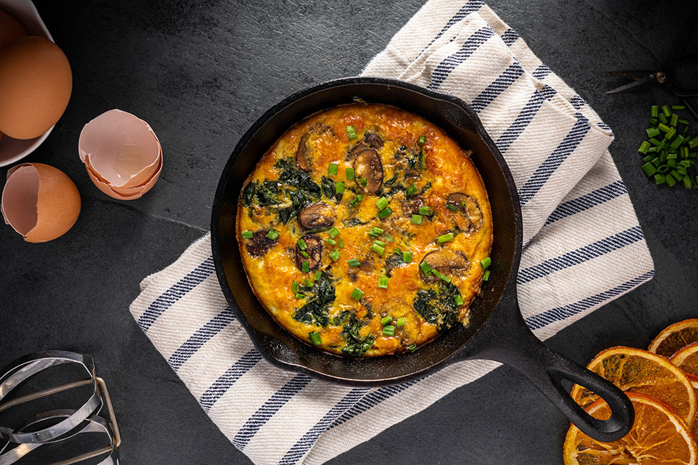 Frittata with spinach, mushrooms, and parmesan cheese garnished with chopped chives viewed from above.