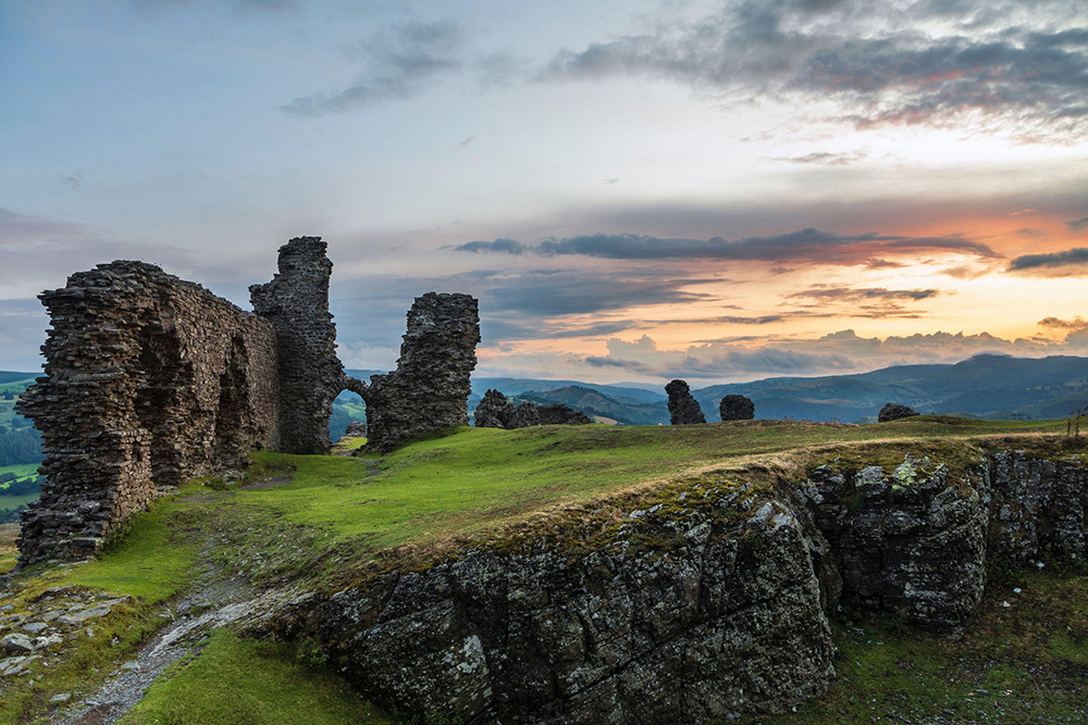 Stone ruins on a hillside with a sunset in the background