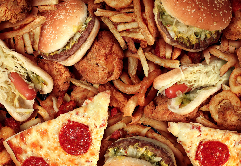 A large group of ultra-processed and fried foods including pizza, burgers, fries, onion rings, and hotdogs