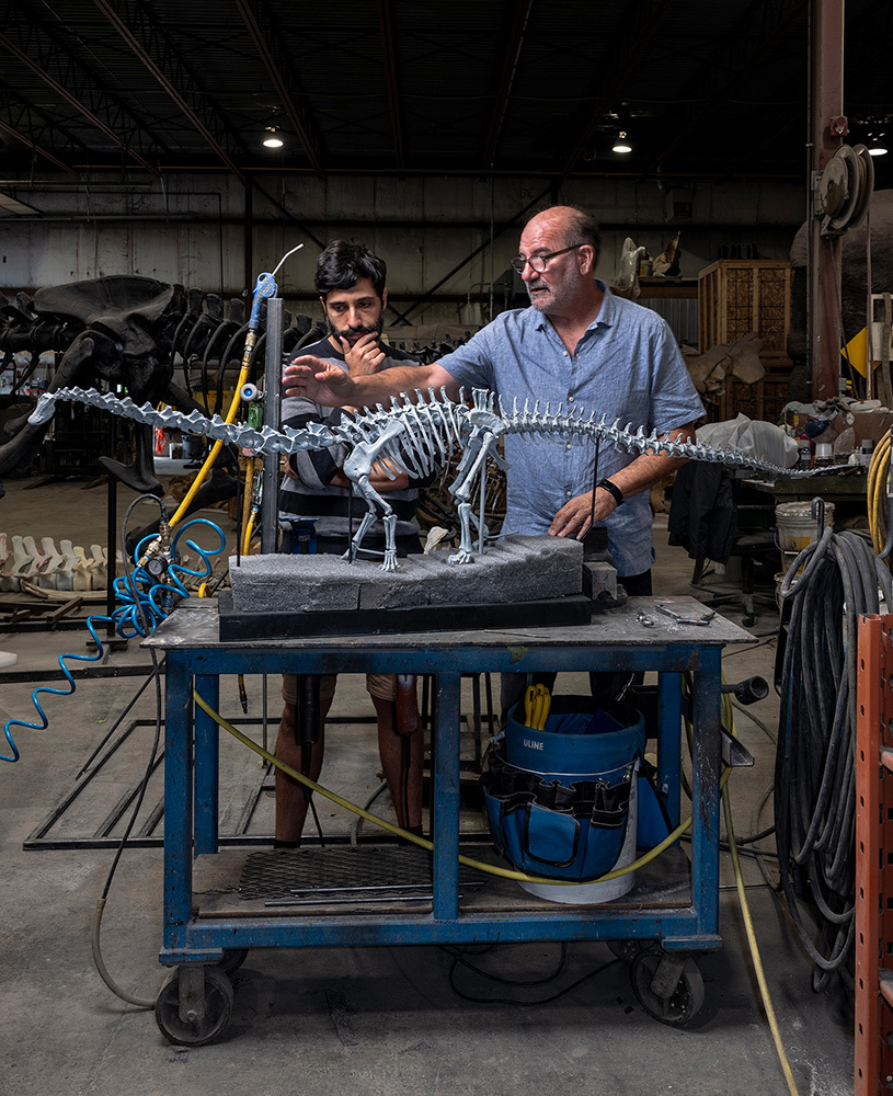 Two men study a medium-sized model of a dinosaur atop a table