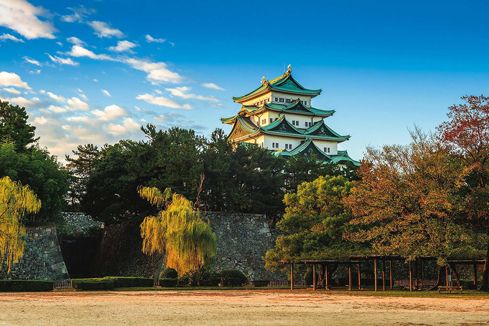 Nagoya Castle, first erected in the 16th century and birthplace of the first great unifier of Japan, Oda Nobunaga, stands above trees with a field in front.