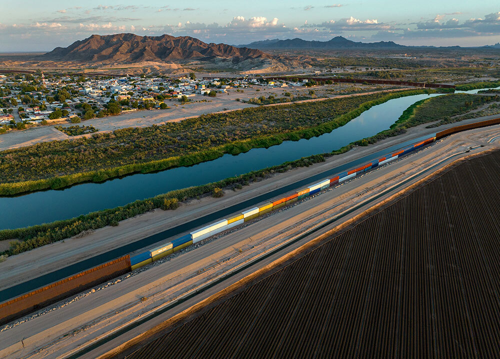 A picture of the border wall between America and Mexico, supplemented with train cars.