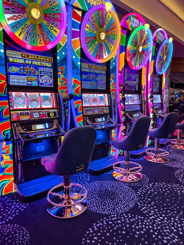 Soft purple seats are empty in front of the bright multi-colored wheels of the slot machine
