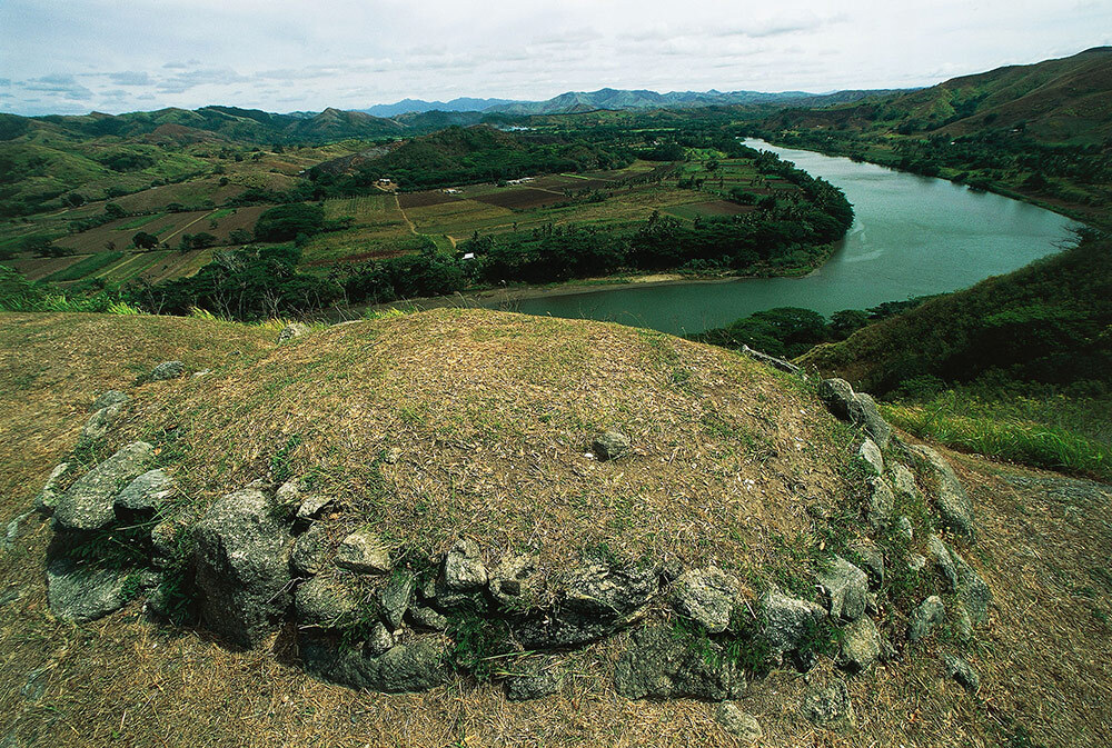 The tomb, a mound of grass with a wall of rocks around it, of the chieftain in Tavuni Hill Fort and the Sigatoka river, Sigatoka Valley, Viti Levu Island, Fiji