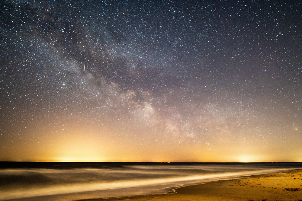 Shooting stars are visible amongst a clear view of the Milky Way over the Baltic Sea