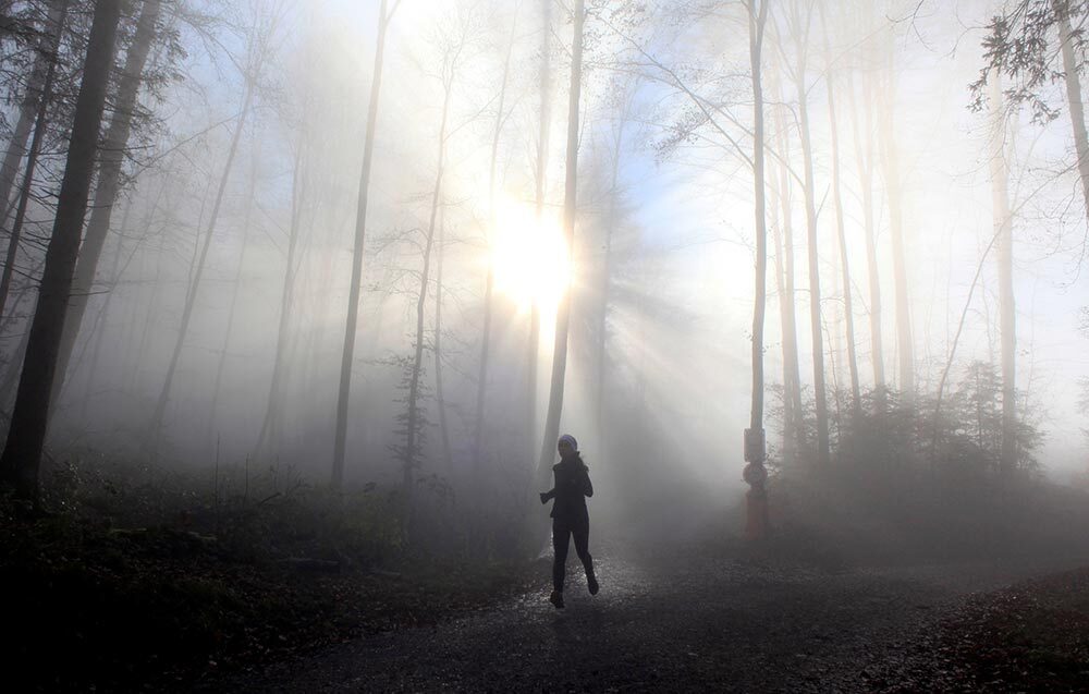 A woman jogs during foggy weather in a forest, in Zurich, Switzerland, 2020.