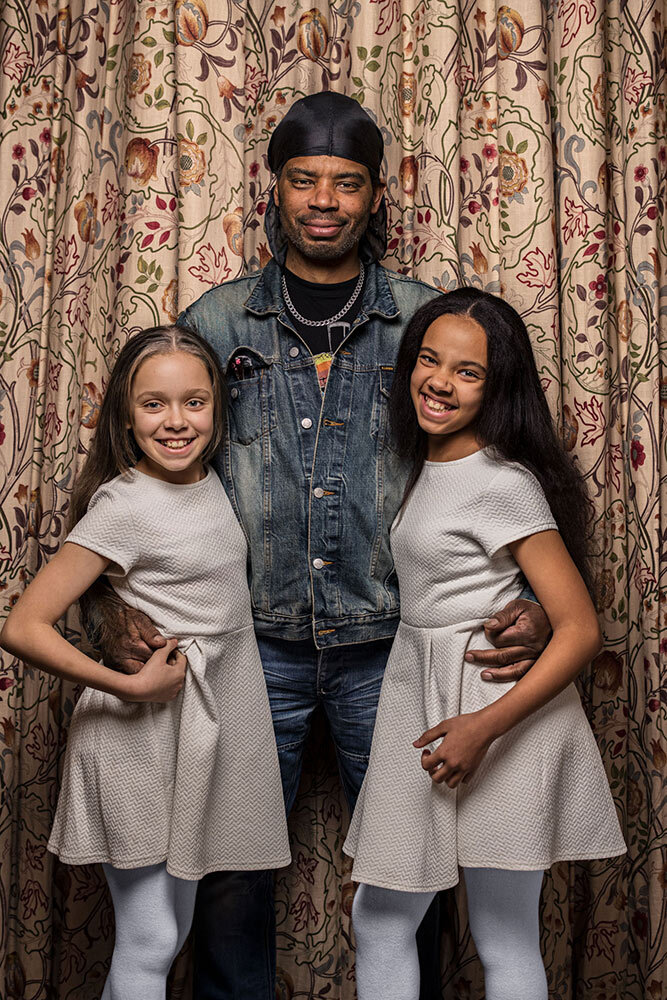 A father stands with his fraternal twin daughters in Birmingham, England