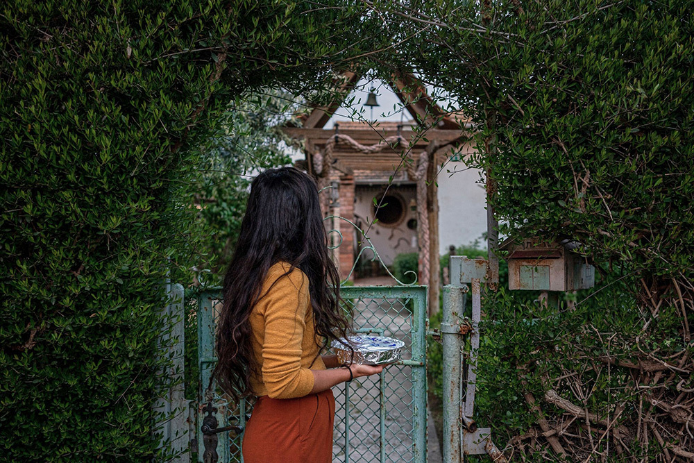 A woman looking through a garden archway holding a steel container