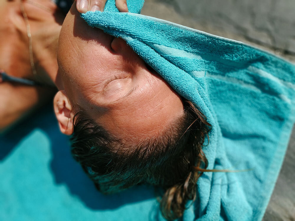 A sunbathing woman blots herself with a towel.