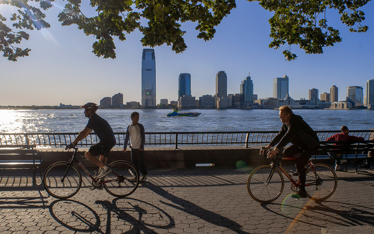 Cyclists overlook New York Harbor and the New Jersey skyline as they pedal around Battery Park.