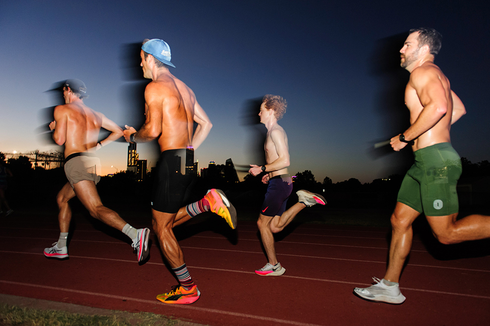 Four men running on a track, dawn light visible on the horizon