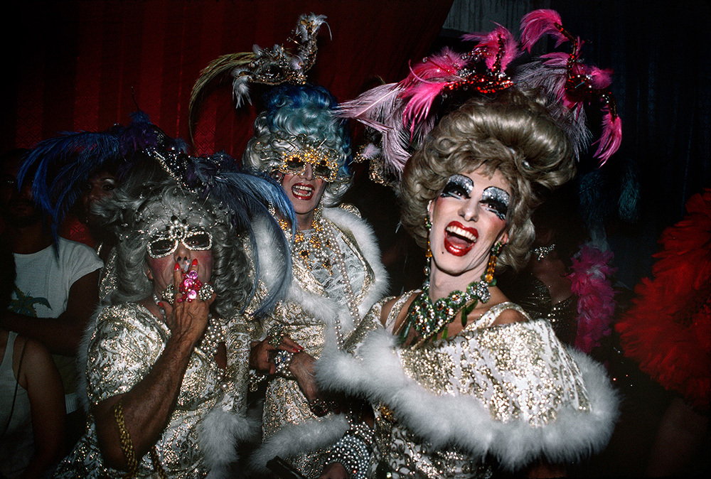 Three people dressed in gowns with large wigs and lots of color