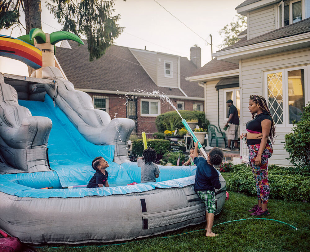 Eden Elder, in gray, splashes among friends and neighbors on an inflatable waterslide in the front yard where his father also played as a boy. The St. Albans home has been in the family for decades.