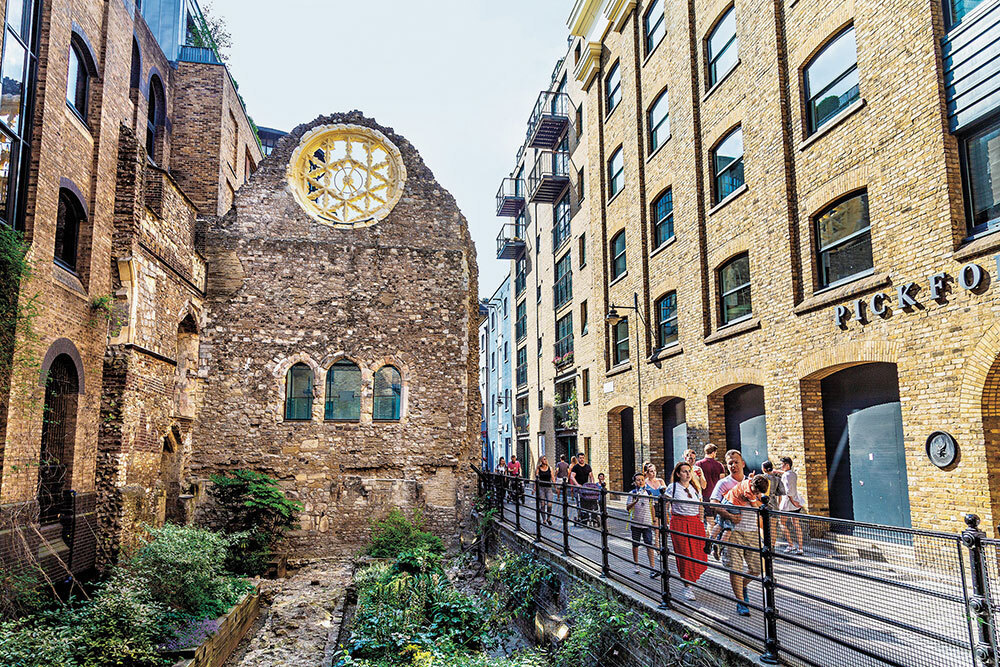 People walk by an old wall with a rose window