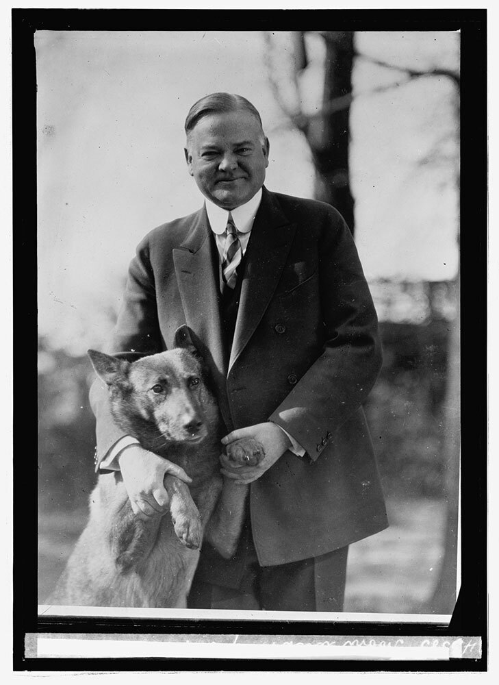 A black and white picture of a man smiling while holding the front paws of a dog