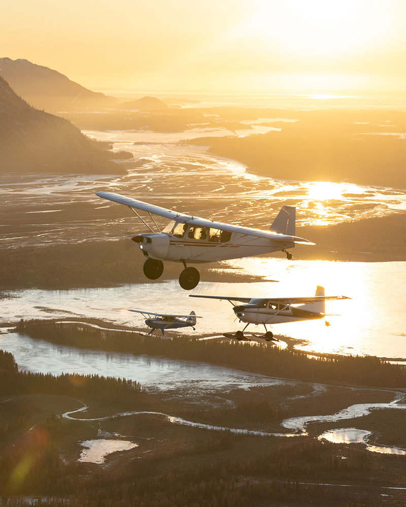 A photo of three small planes flying above a river