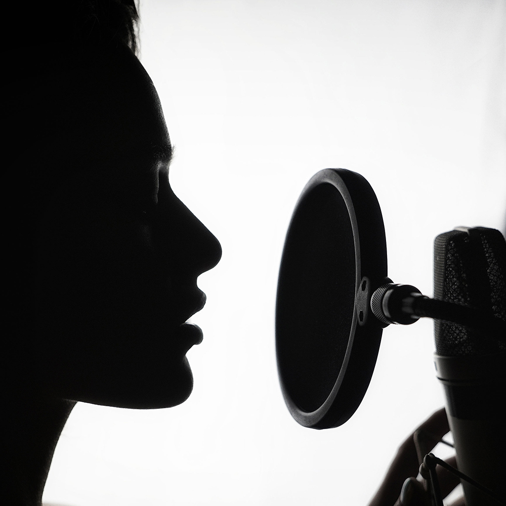 Silhouette of the profile of a woman in front of a microphone in a recording studio