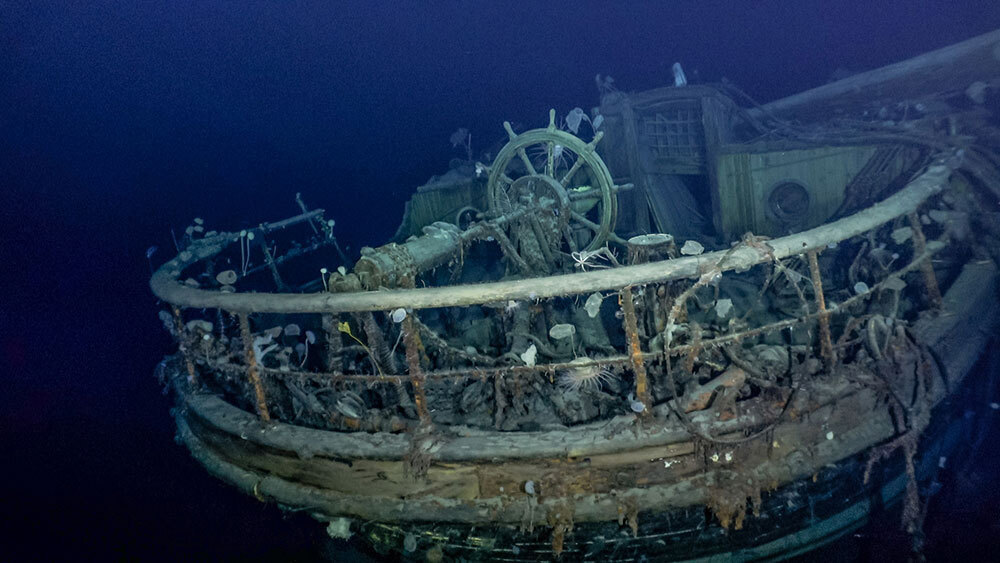 A ship's stern and helm sunk at the bottom of the ocean.