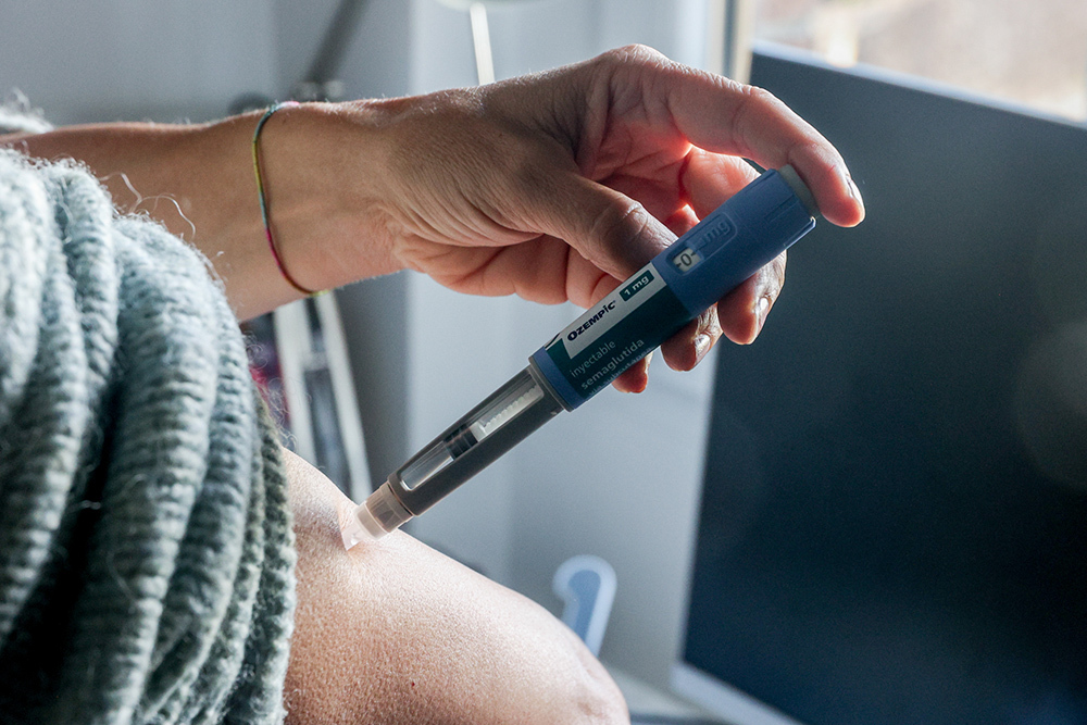 A person using one hand to inject their abdomen using a blue Ozempic multi-dose syringe