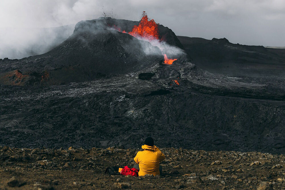 a person in a yellow jacket observes a volcanic eruption from a distance