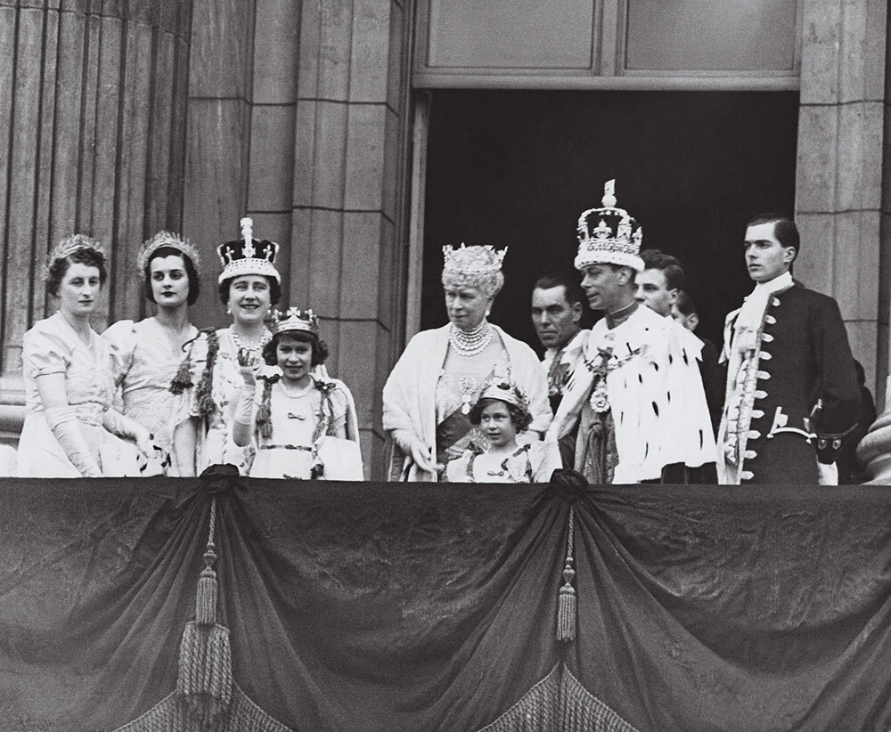 The royal family in crowns looks on from a balcony