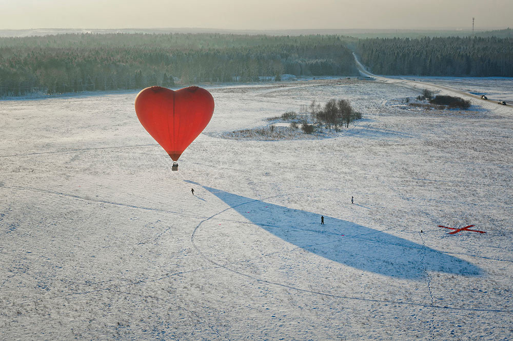 A heart-shaped balloon floats above snow-covered land