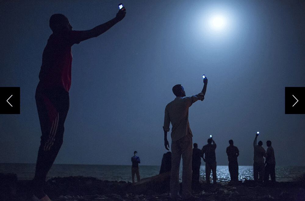 A group of people on a beach at night lifting cell phones up above their heads