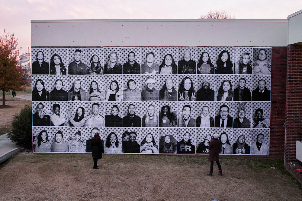 A picture of people looking at a mural made of photograph portraits