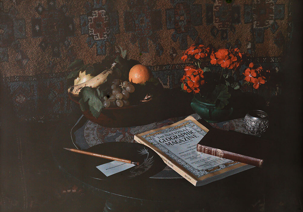 A muted color photograph of a National Geographic magazine on a table with fruit and flowers