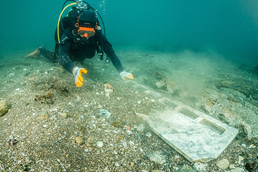 An underwater archaeologist waves away sediment from the remains of a white marble altar in the waters off Puteoli, Italy.