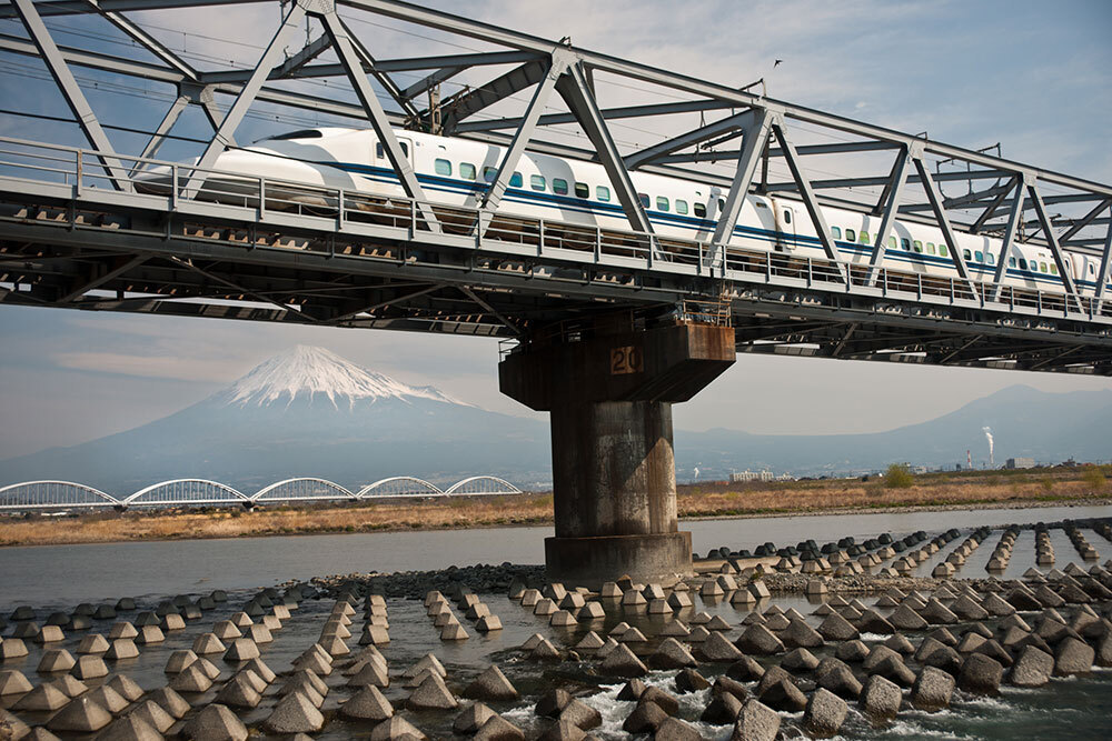 A picture of a train on a bridge with Mount Fuji in the background.