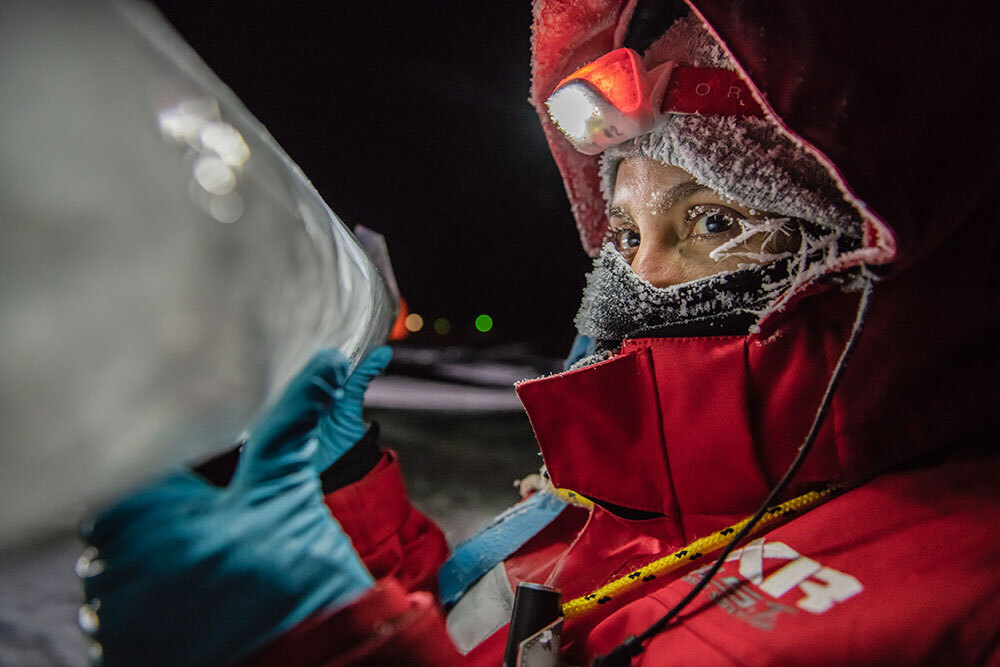 A woman with icicles formed around her face holds a column of ice