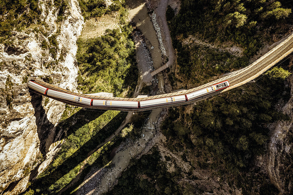 An aerial picture of a train coming out of a tunnel and crossing a valley on a bridge