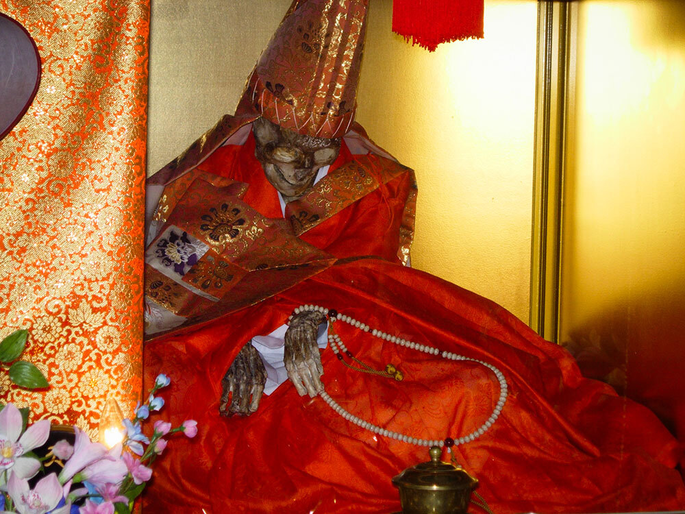 The mummified remains of a monk, dressed in clean ornamental robes and displayed at an altar