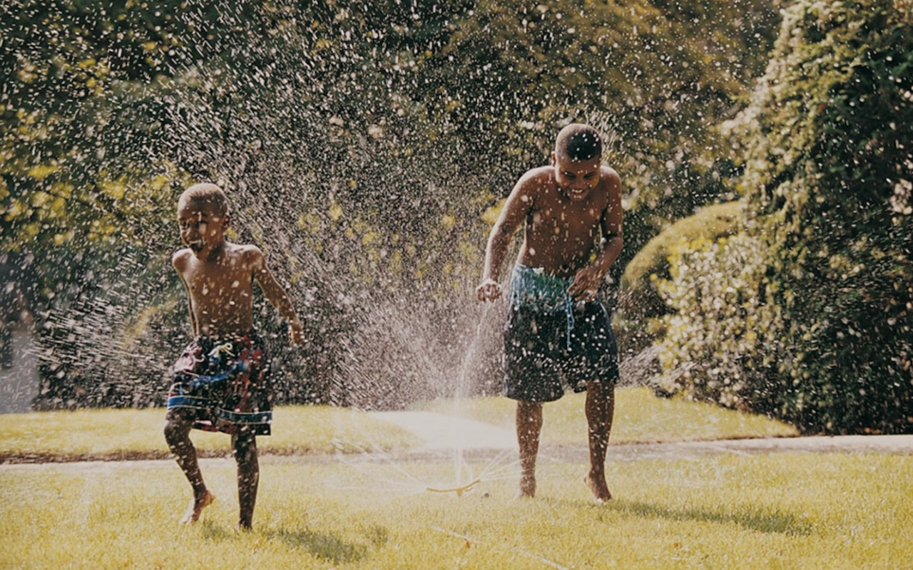 Two boys playing in a water sprinkler in the garden.