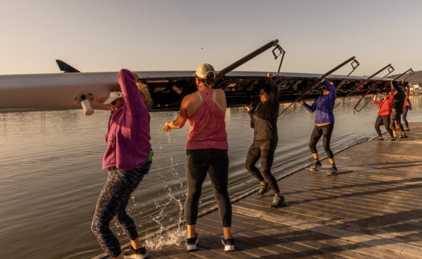 Women rowers lift the eight-boat out of the water and onto their shoulders to bring it back to a boathouse after morning practice.