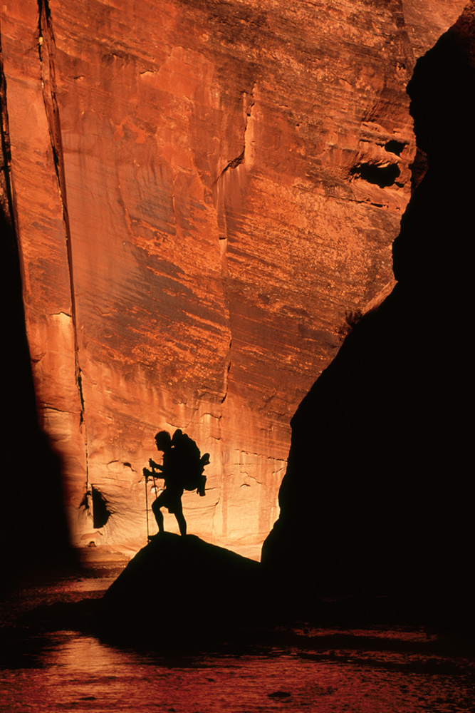 A hiker silhouetted against the orange walls of a slot canyon