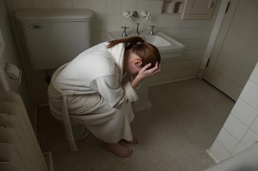 A young woman holds her head in her bathroom.