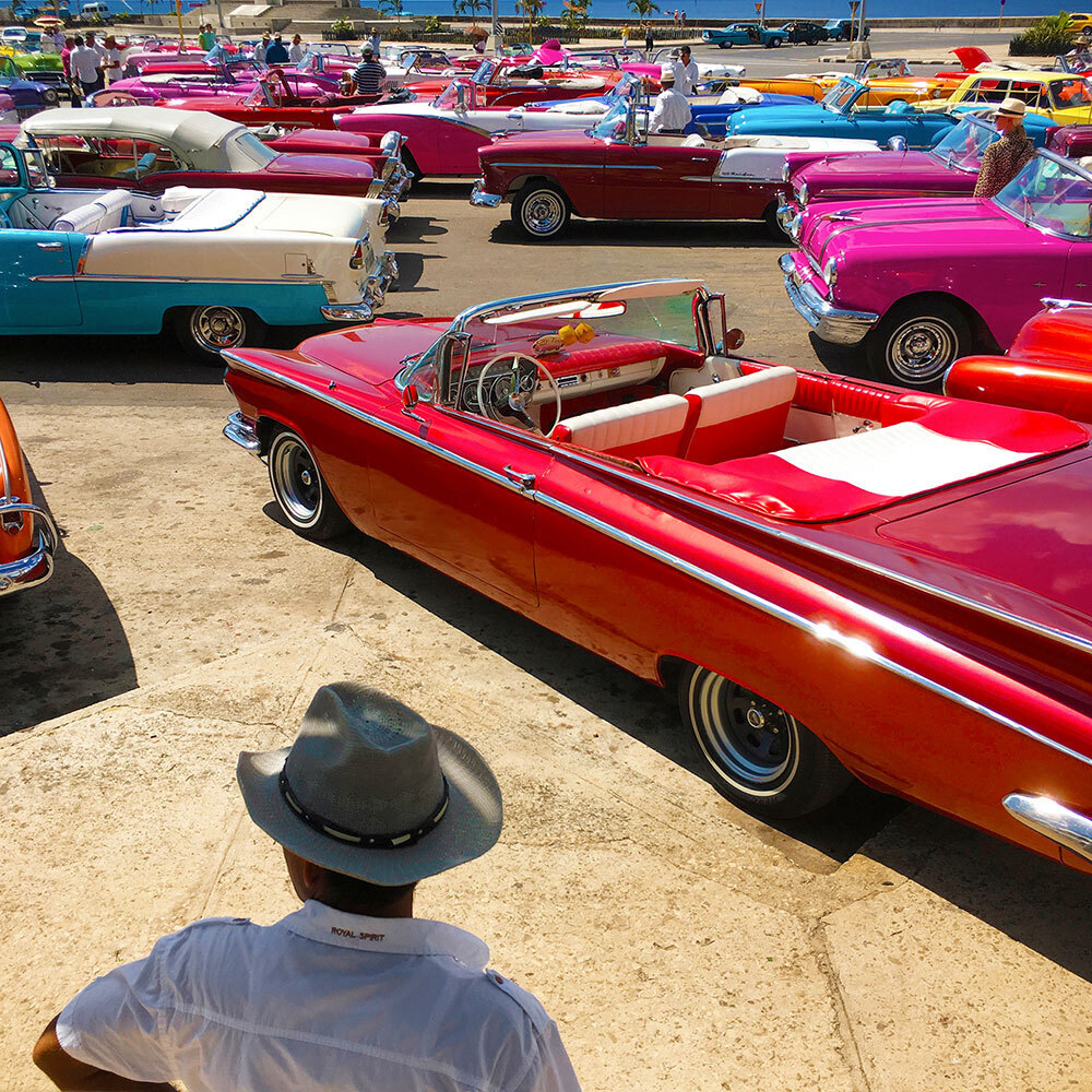 A man in a cowboy hat looks out at a lot full of colorful antique cars