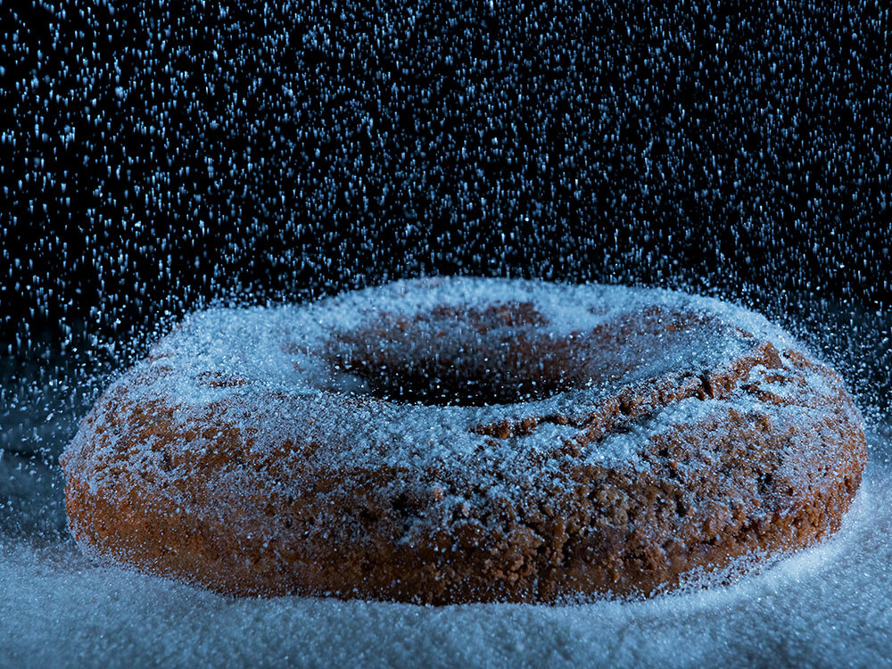 A donut being dusted with sugar