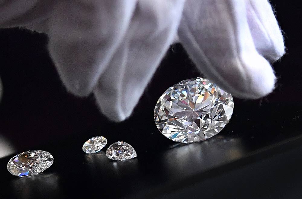 A white gloved hand reaches for several diamonds on a black background