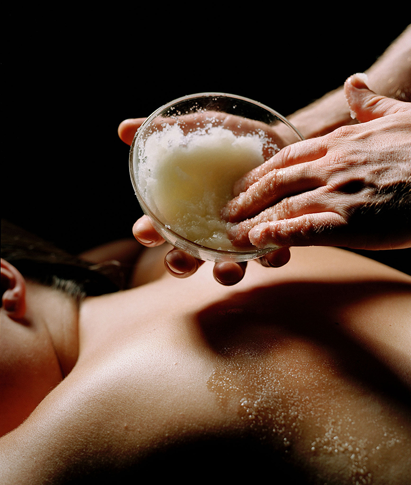 Masseuse giving woman mineral salts treatment on her back with a black background