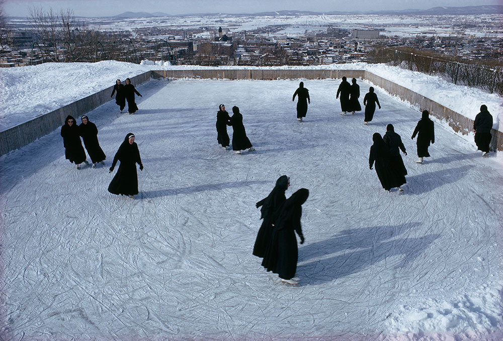 A picture of nuns ice skating with a snowy city in the background