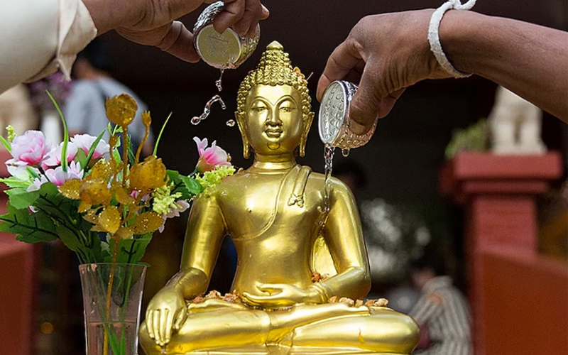 Two people pour water on a Buddha statue.