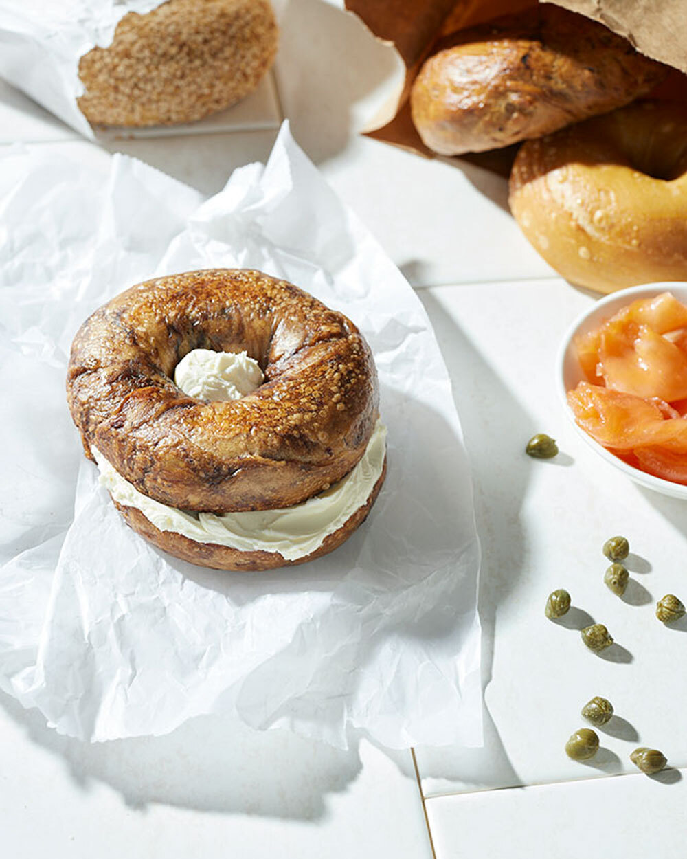 a bagel and some bagel toppings on a white surface