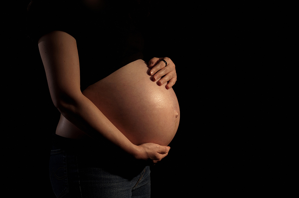 A pregnant woman takes a photograph on a black background