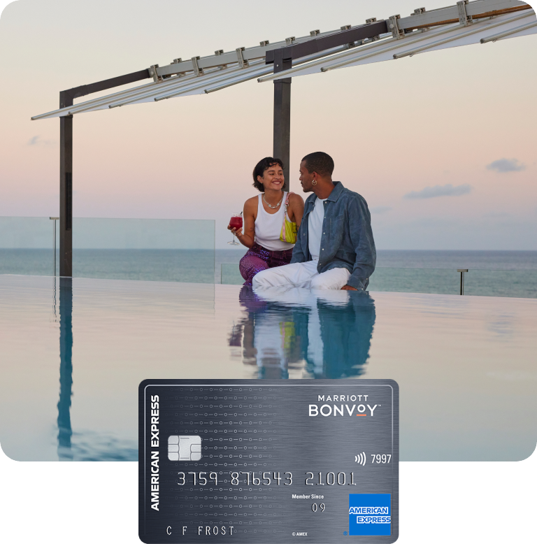 A couple sitting by a luxury seaside hotel's infinity pool in Ibiza, Spain, at sunset.