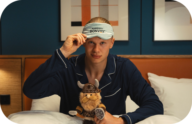 Soccer player Erling Haaland wearing a Marriott Bonvoy eye mask and holding a plush Viking toy.